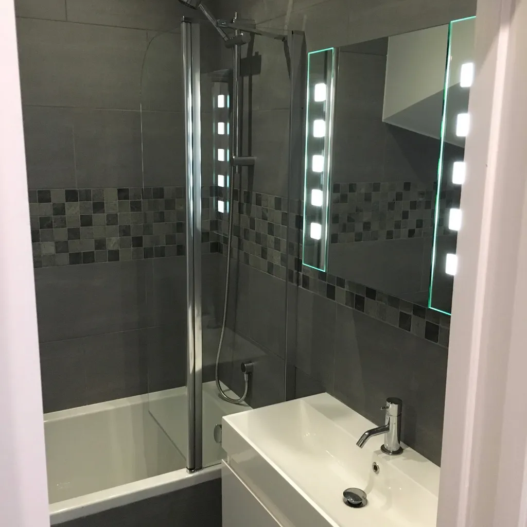 Finished bathroom with grey tiling, mosaic detail and an illuminated mirror
