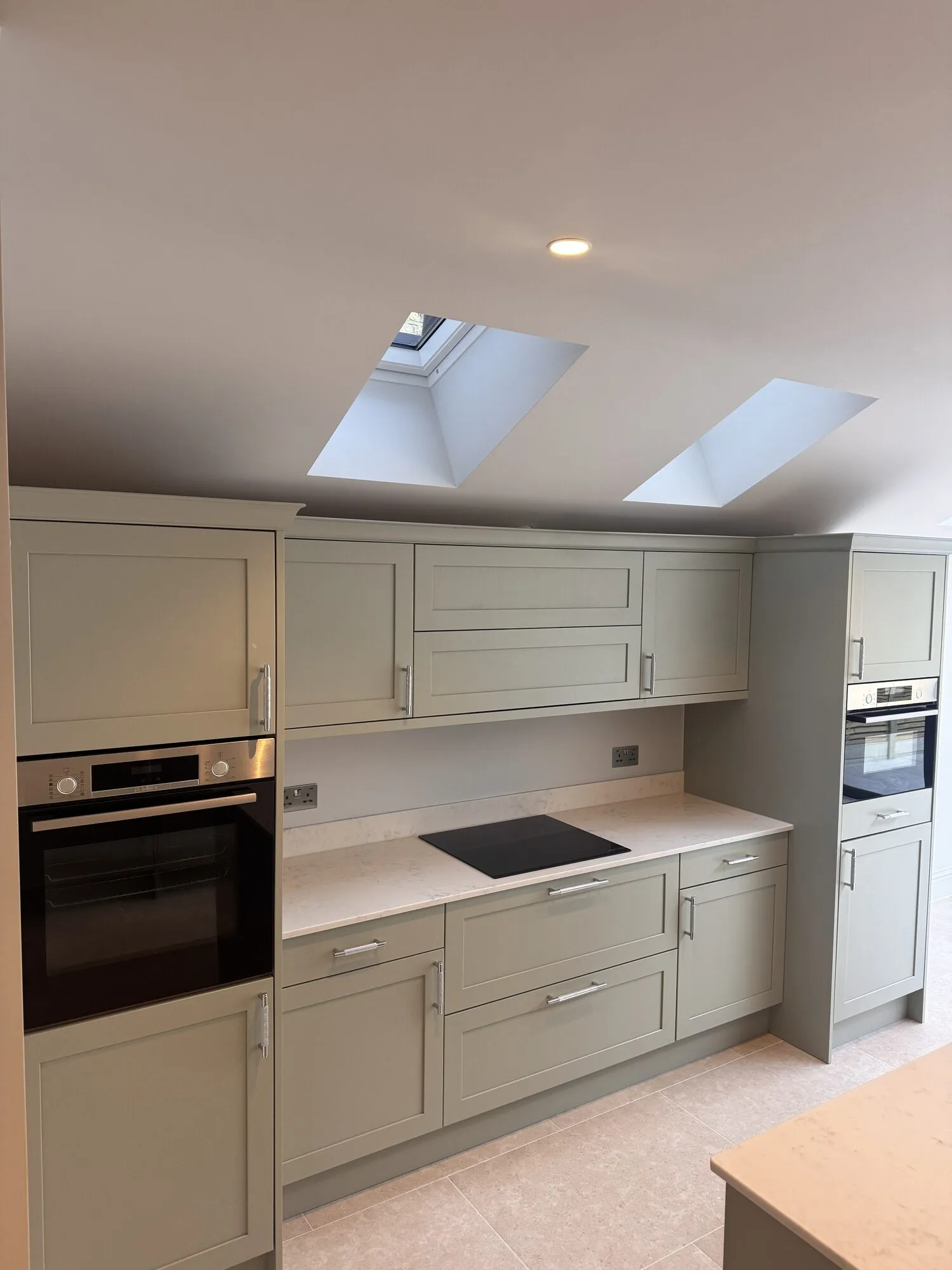 Finished sage green shaker kitchen with quartz worktops, integrated ovens and rooflights above