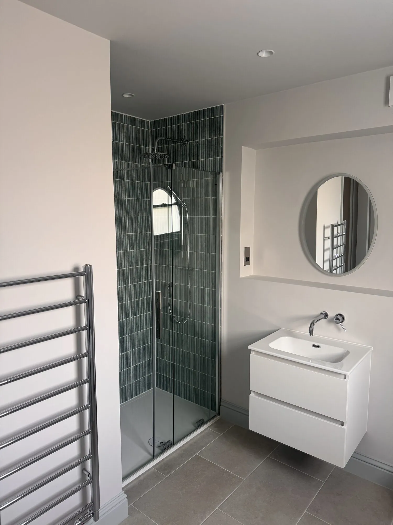 Finished shower room with green fluted tiling, wall-hung basin and round mirror