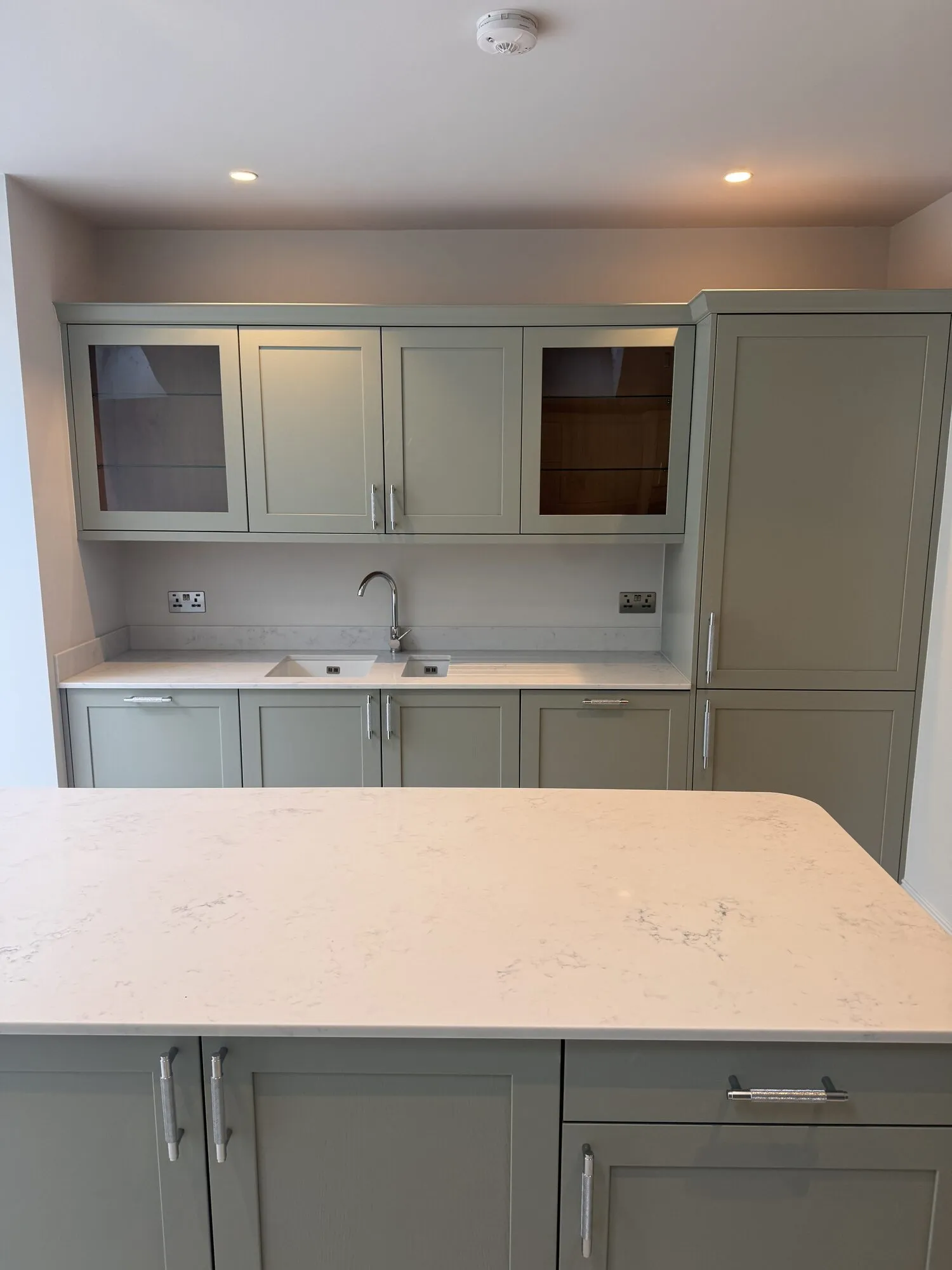 Kitchen sink run with glazed wall cabinets and the quartz island in the foreground