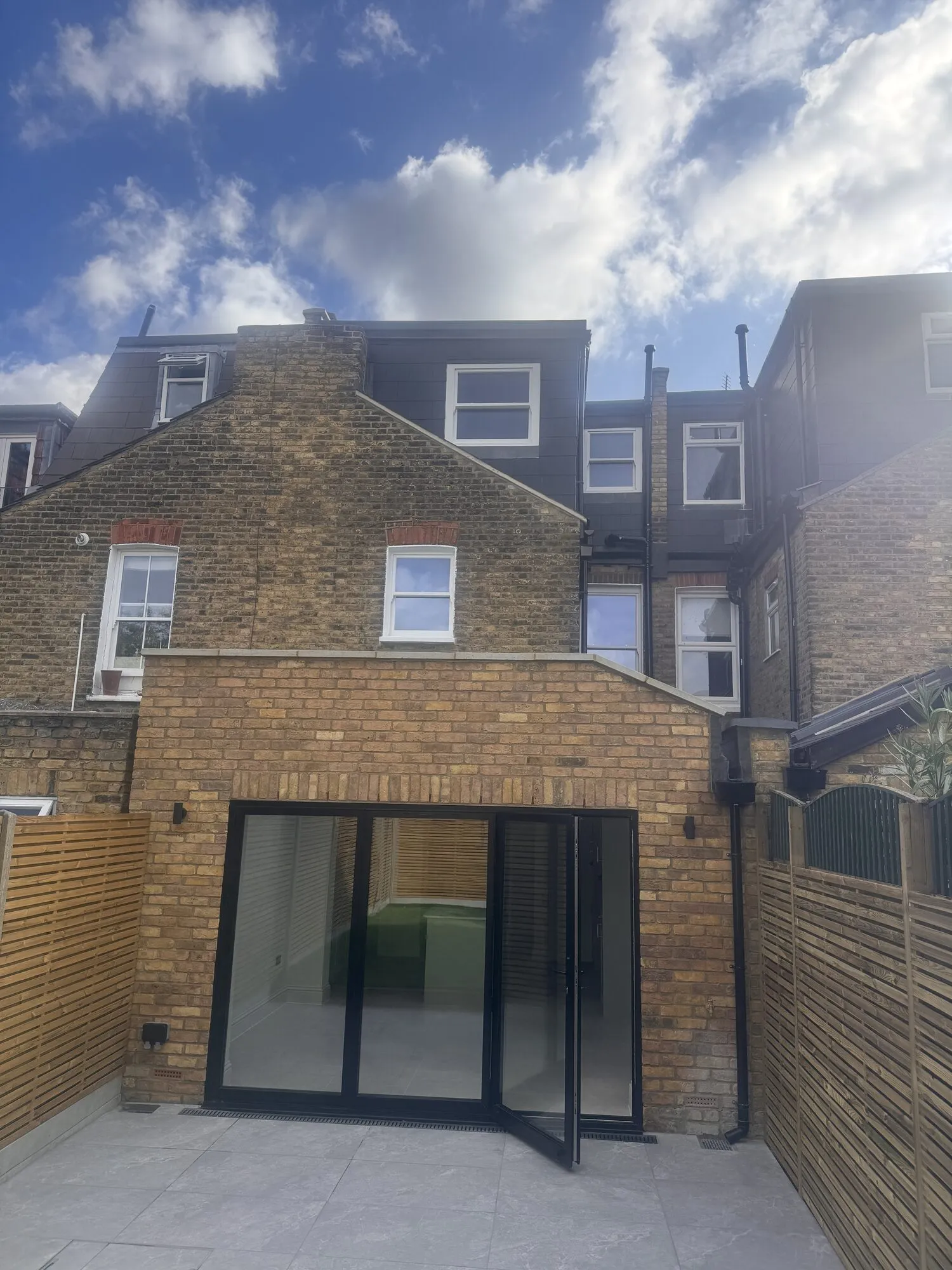 Finished rear extension in matching stock brick with black sliding doors onto a tiled terrace, on an Earlsfield Victorian terrace