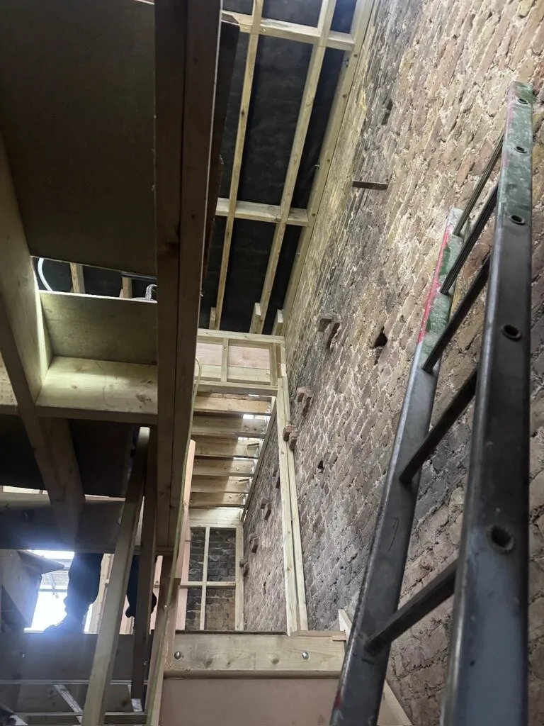 Stairwell and rear return stripped back to exposed brickwork with new timber studwork framing during a full Earlsfield house renovation