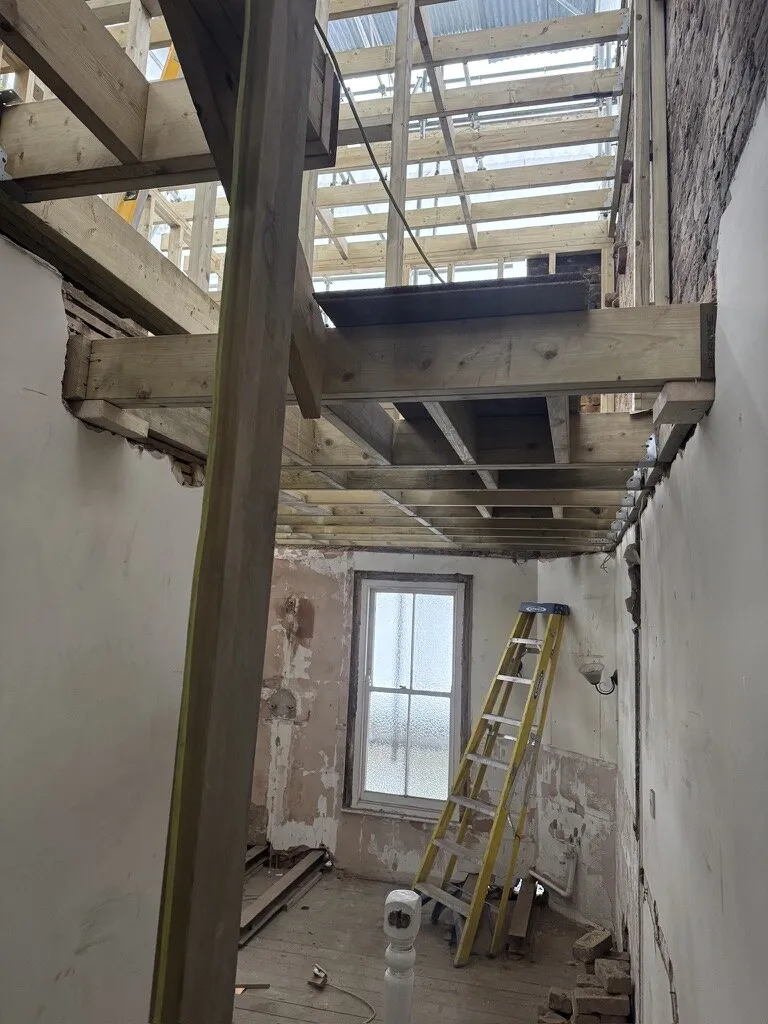New steel beam and timber joists spanning a stripped-out rear room beneath a temporary scaffold roof