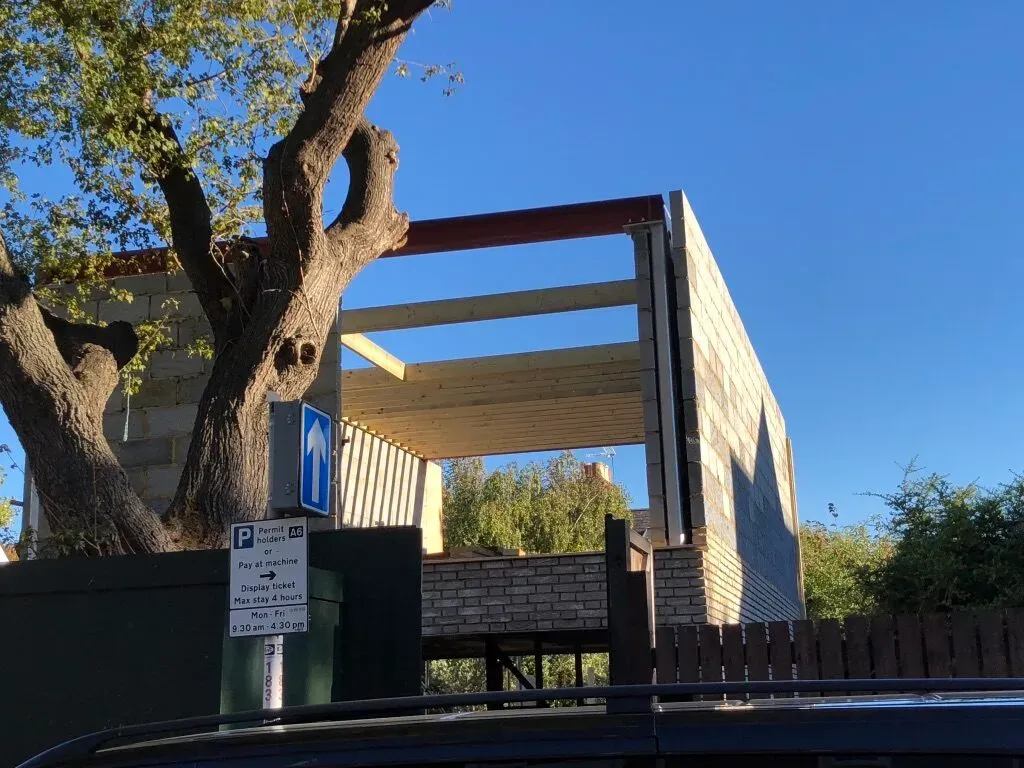 The new-build steel frame and blockwork seen from the garden with a mature tree retained on site