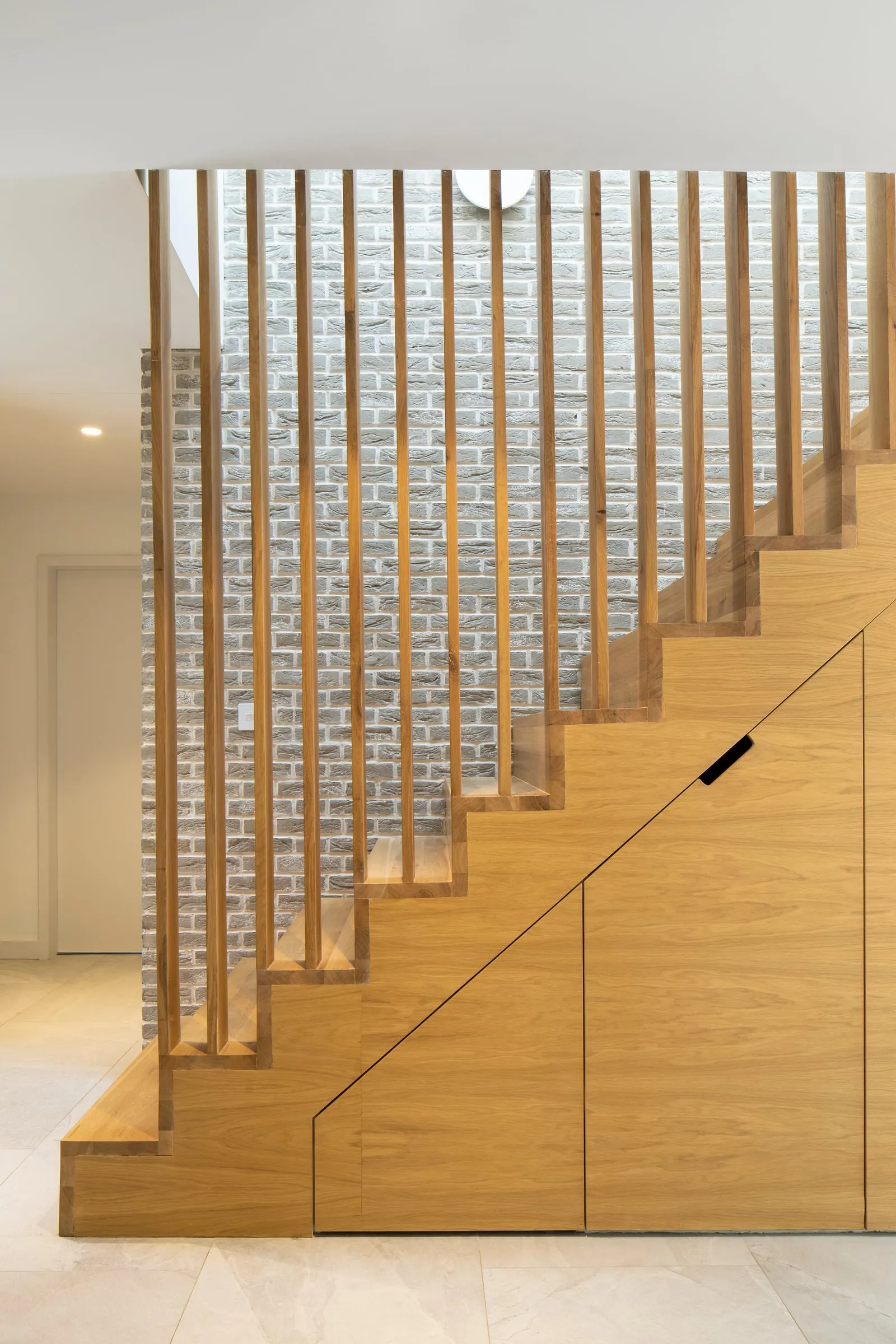 Bespoke oak staircase with vertical timber screen against a brick wall